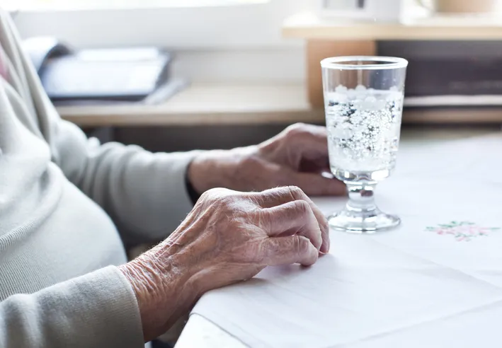 Older adult sitting at a table with a glass of water, illustrating dehydration concerns in long-term care