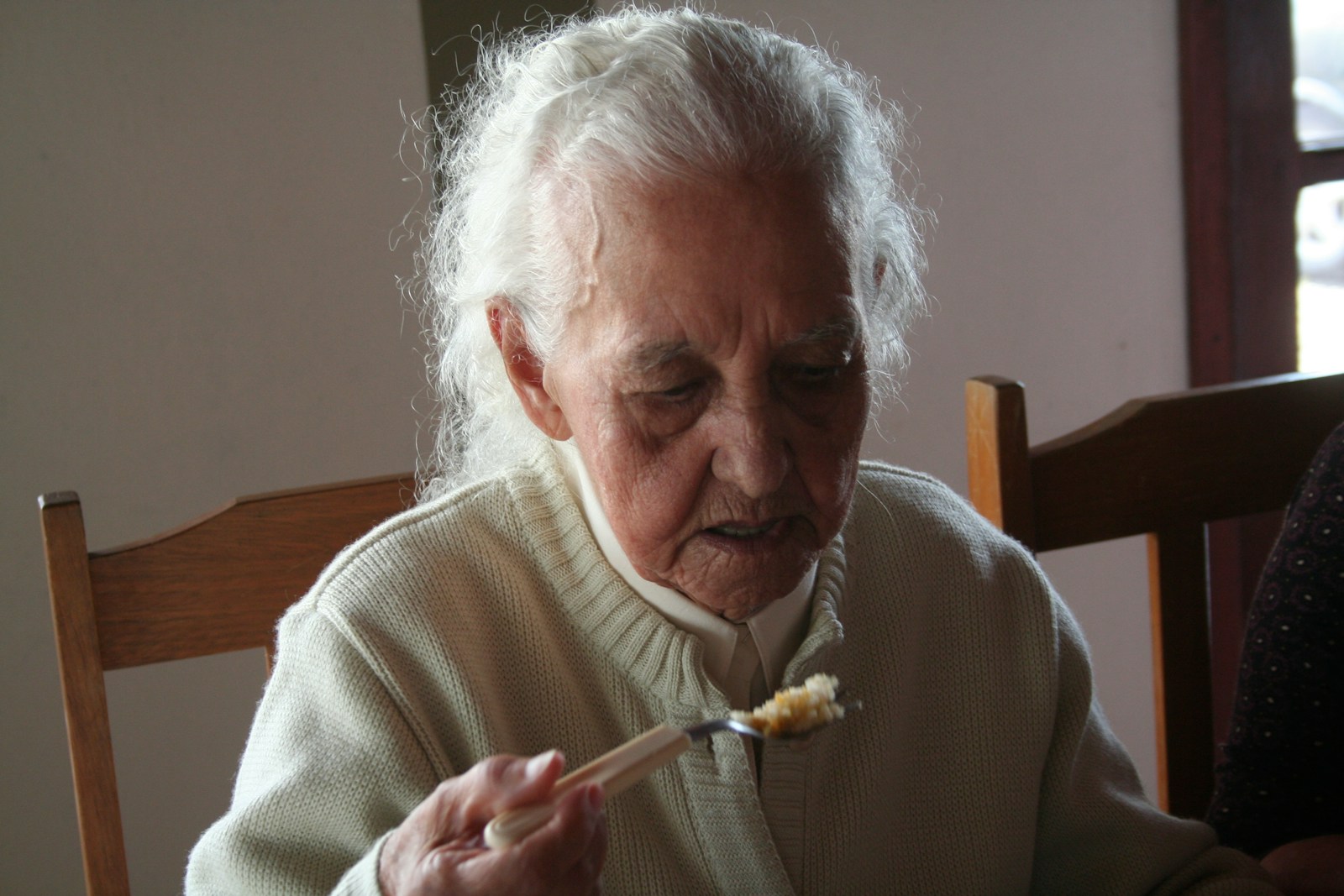 Elderly man in white sweater holding fork